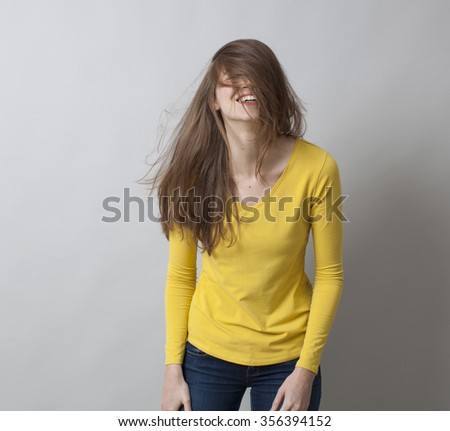 excitement and humor concept - giggling 20s girl messing up her hair for fun,covering her smiling face with her long hair for laughter,studio shot