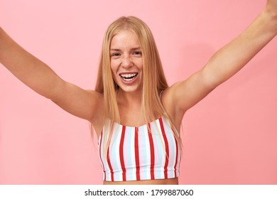 Excitement, Joy And Happiness Concept. Studio Shot Of Beautiful Happy Teenage Girl With Long Fair Hair And Braces Having Excited Look, Smiling Broadly, Hands Up, Glad To See Friend, Going To Give Hug