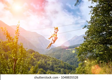 Exciting adventure activity in mountains. Man and woman hanging on a rope-way. Tourists ride on the Zipline through the canyon on blue sky background. Couple in helmets is riding on a cable car - Powered by Shutterstock