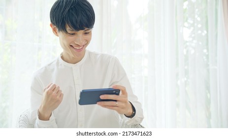 Exciting Asian Man Watching A Smart Phone. Online Sports Broadcast. Social Game.