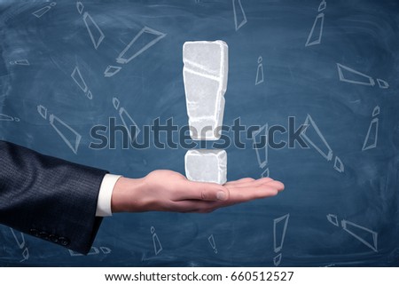 An exclamation mark made of white ice placed on businessman's open palm on chalkboard background. Business solutions. Best and ready answer. Signs and icons.