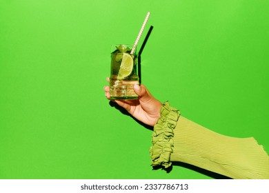 Exclusive alcoholic drink. Female hand holding glass with gin tonik cocktail with lime over bright green background. Concept of copy space for ad, design, drinks, pop art, party and relax. - Powered by Shutterstock