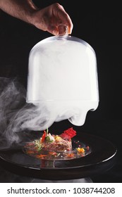 Exclusive Restaurant Food. Chef Lifts Cloche With Liquid Nitrogen And Serves Raw Veal Tartare With Sauce, Quail Egg, Vegetables And Crisp On Black Plate. Organic Healthy Meals In Modern Serving