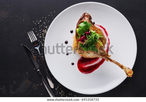 Exclusive\
restaurant meals. Duck confit with braised cabbage, baked apple and\
cranberry sauce served on snow white plate with cutlery on black\
table background, copy space, top\
view