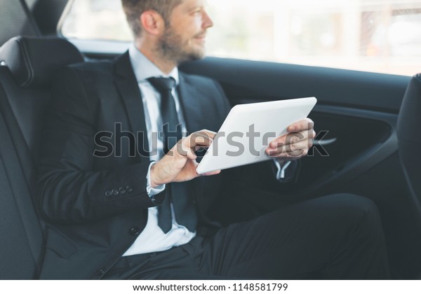 Executive businessman sitting at the back of car\
using a digital\
tablet