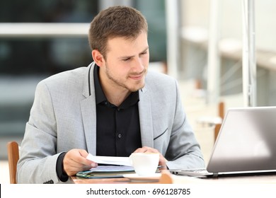 Executive comparing documents on line with a laptop sitting in a coffee shop