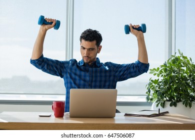 Executive exercising with dumbbells while working on laptop in office