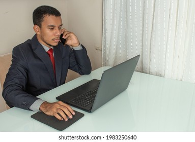 Executive Man Looking At A Computer And Holding A  Cellphone  And A Mouse At The Same Time With A Cup Of Cofee Under The White Table At The Office