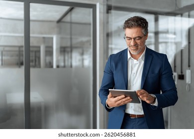 Executive man in suit working using computer for financial business banking work. Smiling senior mature Indian or Latin entrepreneur businessman looking at digital tablet screen in office. Copy space 