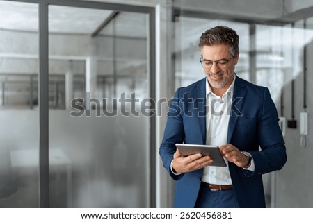 Executive man in suit working using computer for financial business banking work. Smiling senior mature Indian or Latin entrepreneur businessman looking at digital tablet screen in office. Copy space 