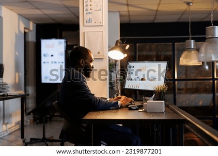 Executive manager analyzing marketing statistics working at financial growth report late at night in startup office. African american employee planning company strategy to increase business profit