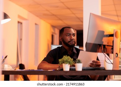 Executive manager analyzing paperwork report and taking notes to create research presentation in office with big windows. Working on project data with documents and computer during sunset. - Shutterstock ID 2174911863