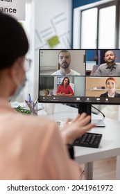 Executive manager with medical face mask discussing management statistics with remote team having online videocall meeting conference on laptop working in startup office. Teleconference on screen - Shutterstock ID 2041961972