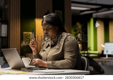 Executive manager works after hours at her desk, playing with a pen while envisioning a tactical solution, evaluating options and using critical thinking to gain a different perspective