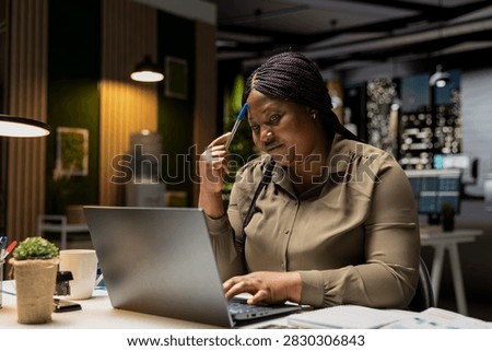Executive manager works after hours at her desk, playing with a pen while envisioning a tactical solution, evaluating options and using critical thinking to gain a different perspective