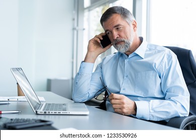 Executive senior businessman using his mobile phone and talking wih somebody while working laptop in the office