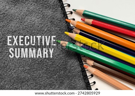 Executive summary text on notebook with colored pencils on dark background.
