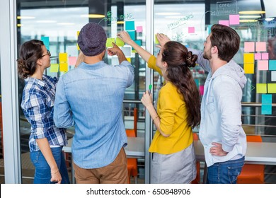 Executives Discussing Over Sticky Notes On Glass Wall In Office