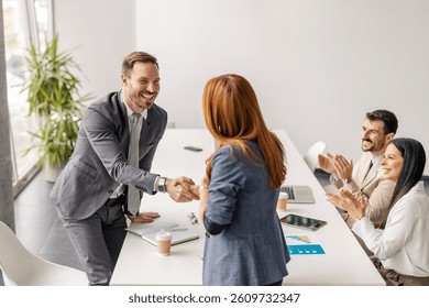 Executives shaking hands on congratulating on achievement while gender balanced team members clapping hands.