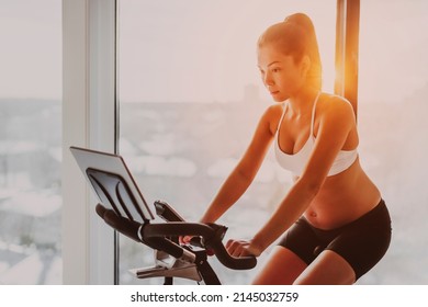 Exercise bike Asian woman training during pregnancy. Workout at home fitness gym watching online cycle class on stationary bicycle