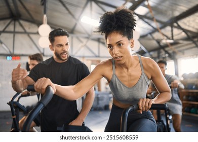 Exercise bike, motivation and personal trainer with a black woman in gym for exercise or fitness. Wellness, training and cycling with a female and coach working together in a health or wellness club - Powered by Shutterstock