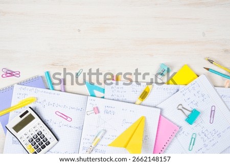 Exercise book white sheets with formulas, multicolor office supplies and calculator on wooden table background with space for text. NO AI USED