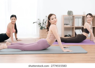 Exercise class in bright studio, three women doing yoga pose on mat, calm fitness practice with stretching and healthy lifestyle
