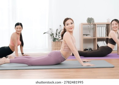 Exercise class in bright studio with three women doing yoga stretch on mat, calm and healthy fitness practice
