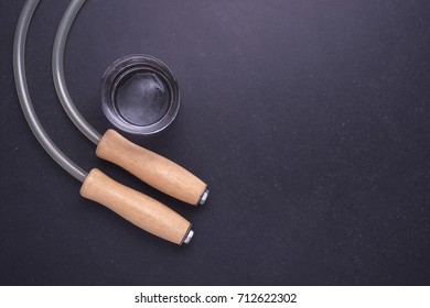 Exercise Concept : Top View Skipping Rope And Glass Cold Water On Black Stone Table Background. Empty Space For Text Or Design