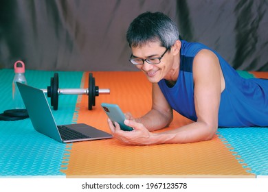 Exercise at home. Senior man happily talking smartphone while watching online class on the laptop in the living room. Exercise in living room. - Powered by Shutterstock