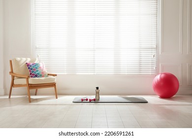 Exercise mat, dumbbells, bottle and fitness ball near armchair in spacious room - Powered by Shutterstock