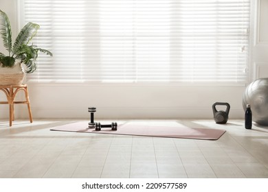 Exercise mat, dumbbells, kettlebell, fitness ball and bottle near window in spacious room - Powered by Shutterstock