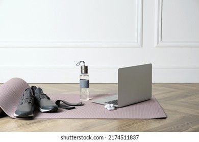 Exercise Mat, Laptop, Bottle Of Water, Wireless Earphones, Fitness Elastic Band And Shoes On Wooden Floor Indoors