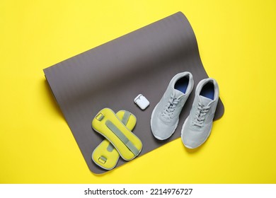 Exercise Mat, Weights, Wireless Earphones And Shoes On Yellow Background, Top View