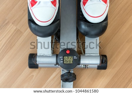 Exercise on a stepping machine, looking from above. Active person with sport shoes exercising on stepper on wooden floor, close up.