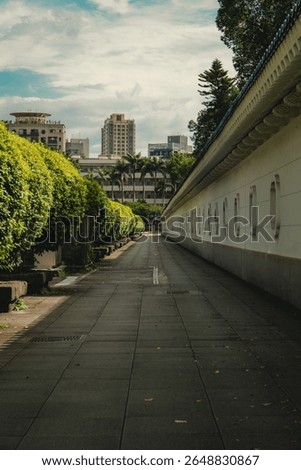The exercise path is straight along the wall and there are green bushes along the way In Taiwan there are buildings behind the beautiful sky The sun is hot outside