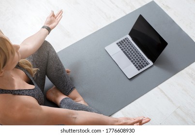 Exercise and relaxation. Woman in lotus position sits on mat on floor with laptop with empty screen, cropped, copy space - Shutterstock ID 1776608930