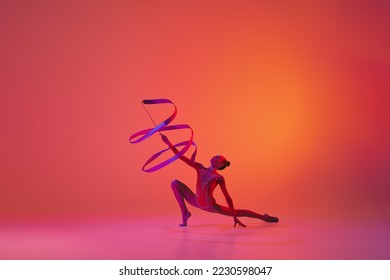 Exercise with ribbon. Young flexible teen girl rhythmic gymnast in motion, action isolated over pink background in neon light. Sport, beauty, competition, flexibility, active lifestyle. Performance - Powered by Shutterstock