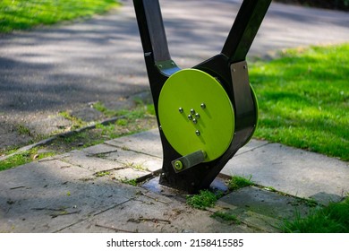 An Exercise Spin Bike Placed In A Public Park. Manual Exercise Bike For Passers By To Cycle On. Next To The Footpath And Green Grass. Sunny Spring Day. No People. Concept For Fitness And Wellbeing.