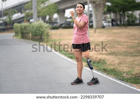Exercise walking Asia woman with prosthetic leg and drink pure water in plastic bottle at the park city	
