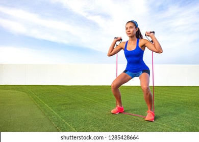 Exercise Woman With Fitness Elastic Band Workout In Outdoor Gym . Asian Girl Doing Resistance Training Outside On Grass. Fit People Lifestyle. Squat And Shoulder Press With Elastics.