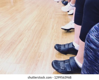 Exercise Women With Cycling Shoes In Row Against Wooden Floor At Fitness Gym. Close Up Queue Of Women Waiting To Joy Cycling Class At Fitness Room. Copy Space