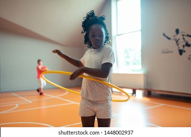 Exercising in class. Concentrated schoolgirl twirling a hula hoop training in the gym with her classmates. - Powered by Shutterstock