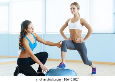 Exercising with fitness ball. Beautiful young woman in sports clothing exercising with personal trainer - Powered by Shutterstock