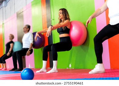 Exercising group doing wall squats with stability balls, an effective gym workout for fitness and strength