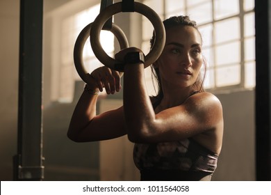Exercising Woman Holding Gymnast Rings And Looking Away. Female Taking Rest After Intense Dip Ring Workout At Gym.