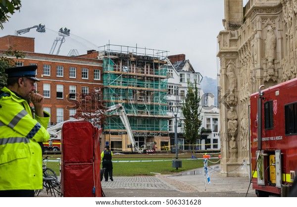 Exeter, Devon, England,\
UK - 29 October 2016: Concerned policeman at the Cathedral green\
look at what is left of the oldest hotel in England, Royal Clarence\
Hotel. 
