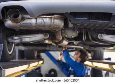 Exhaust of a car on the bridge at a auto repair shop with a mechanic underneath