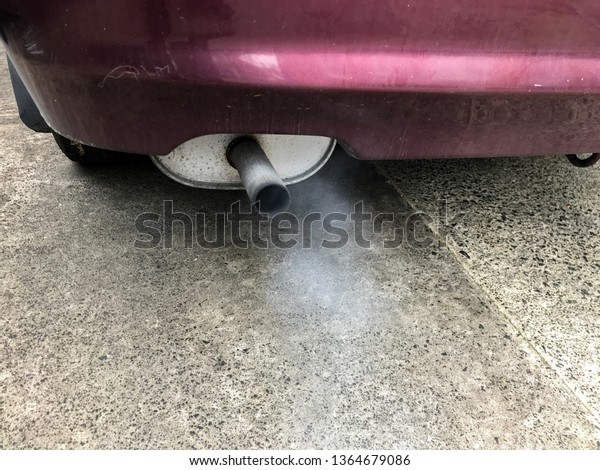 Exhaust fumes emissions from the tail pipe of a\
burgundy car