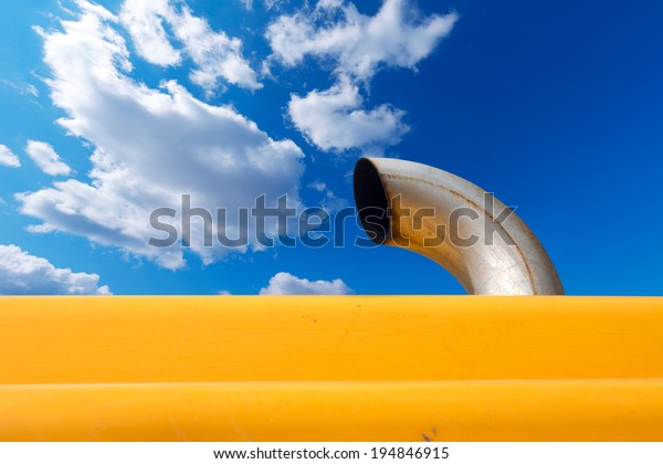 Exhaust Pipe on Blue\
Sky / Detail of an metallic exhaust pipe of an orange excavator on\
blue sky with clouds